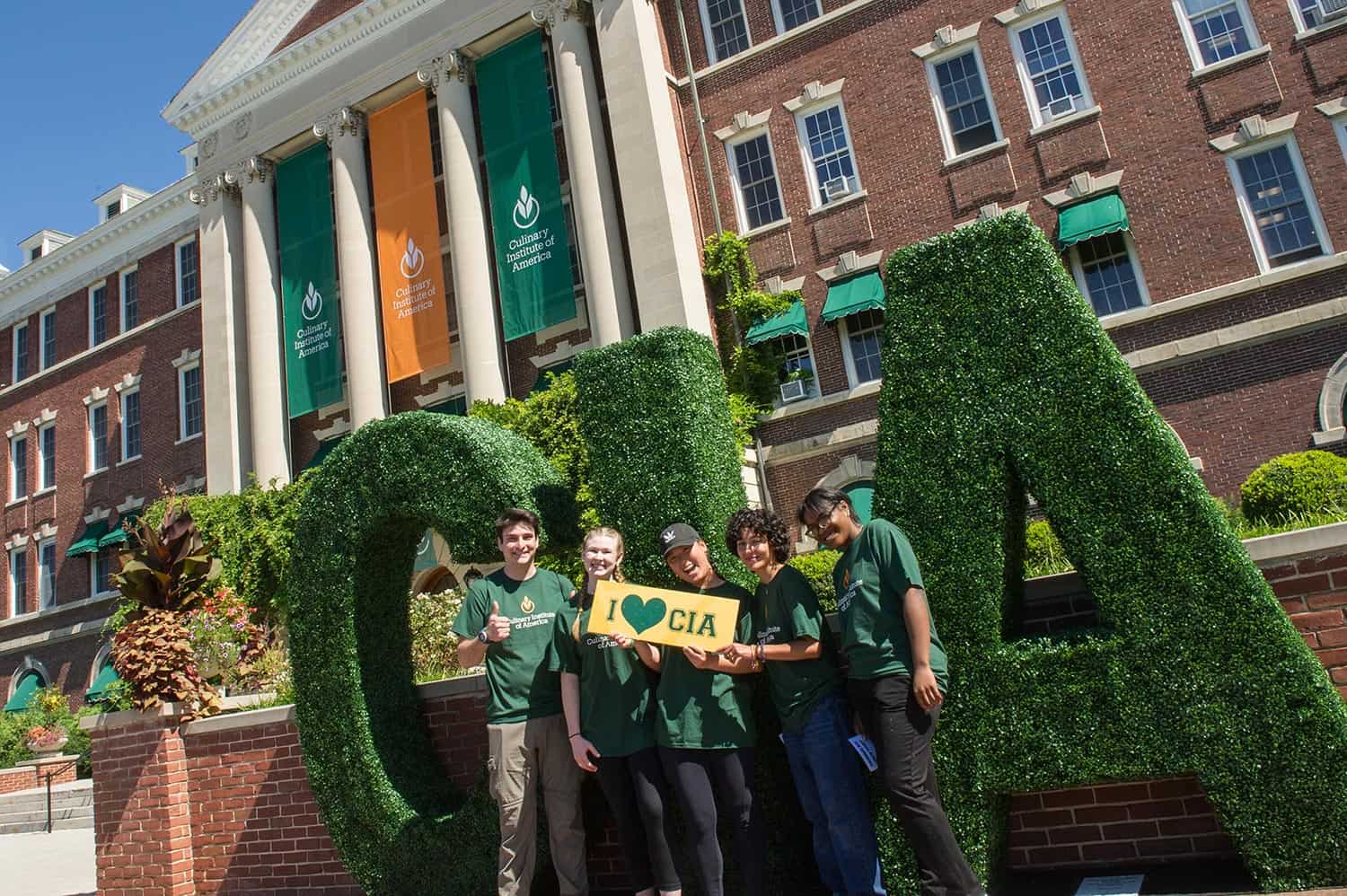 Students visit at a CIA Open House in New York holding a sign 'I heart CIA' in front of Roth Hall.